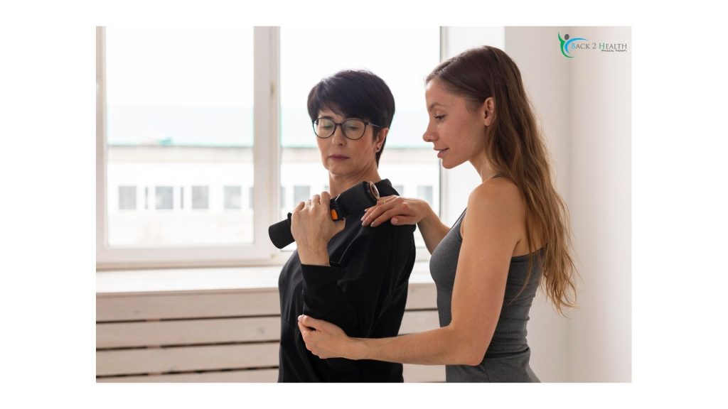 A physical therapist at Back 2 Health guides a patient through a rotator cuff repair protocol rehab exercise. The therapist is providing manual support to the patient's arm and shoulder as the patient performs a controlled lift with a small weighted bar near a bright window.
