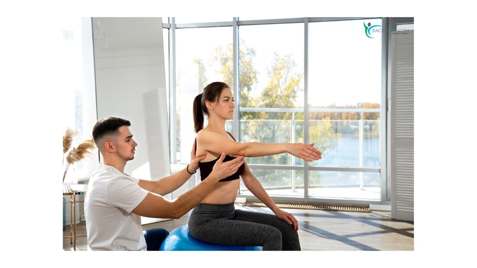 A physical therapist supporting a woman's shoulder blade as she extends her arm forward while sitting on a exercise ball at Back 2 Health physical therapy.